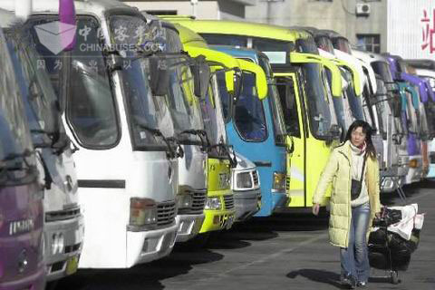 一位回家的旅客經(jīng)過停靠在汽車站里整裝待發(fā)的大客車前